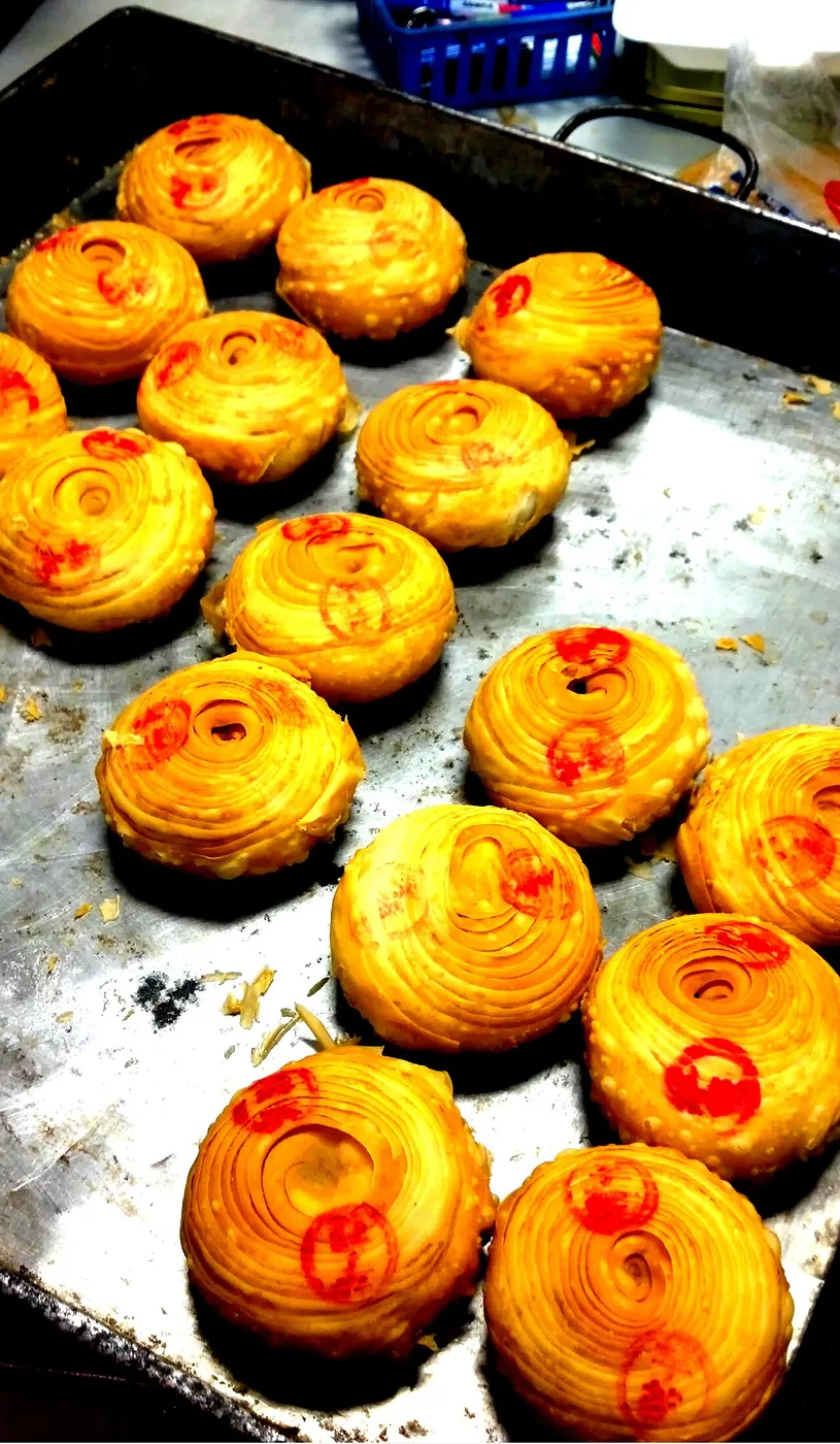 烤盘上刚出炉的潮州月饼，圆形、表面螺旋纹、中心点红