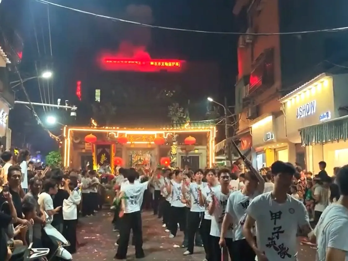 夜裡紅牌樓下，白 T 恤隊伍走過，地上落滿紙屑