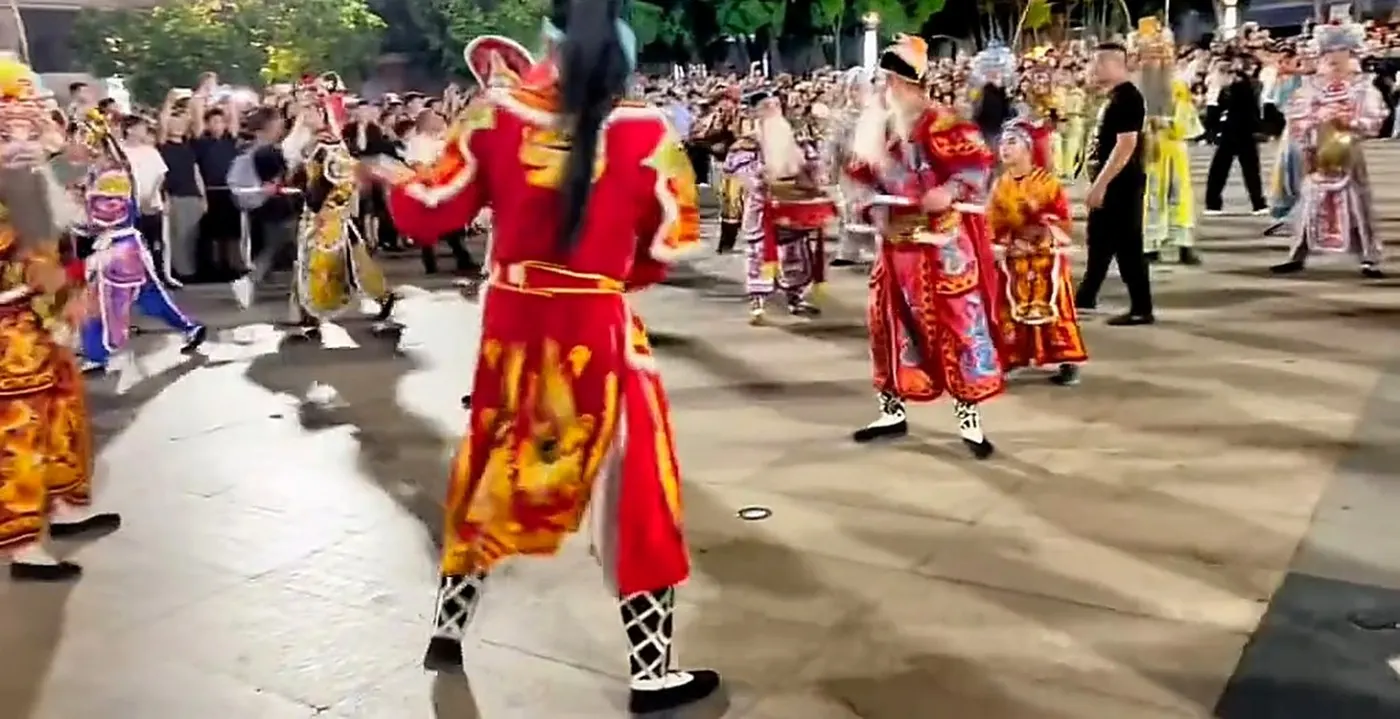 街心一支英歌队迎面推来，队员着彩色戏服、执双槌，两侧挤满围观的人