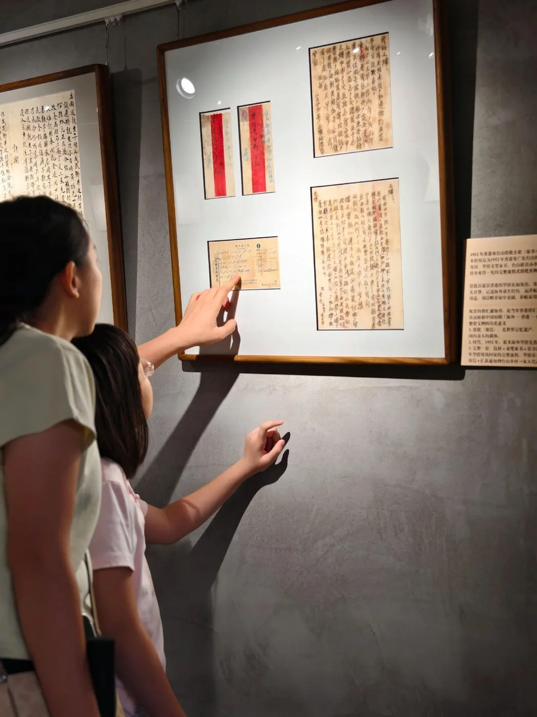 展厅内观众抬手点看墙上的展板，展板内嵌数封侨批