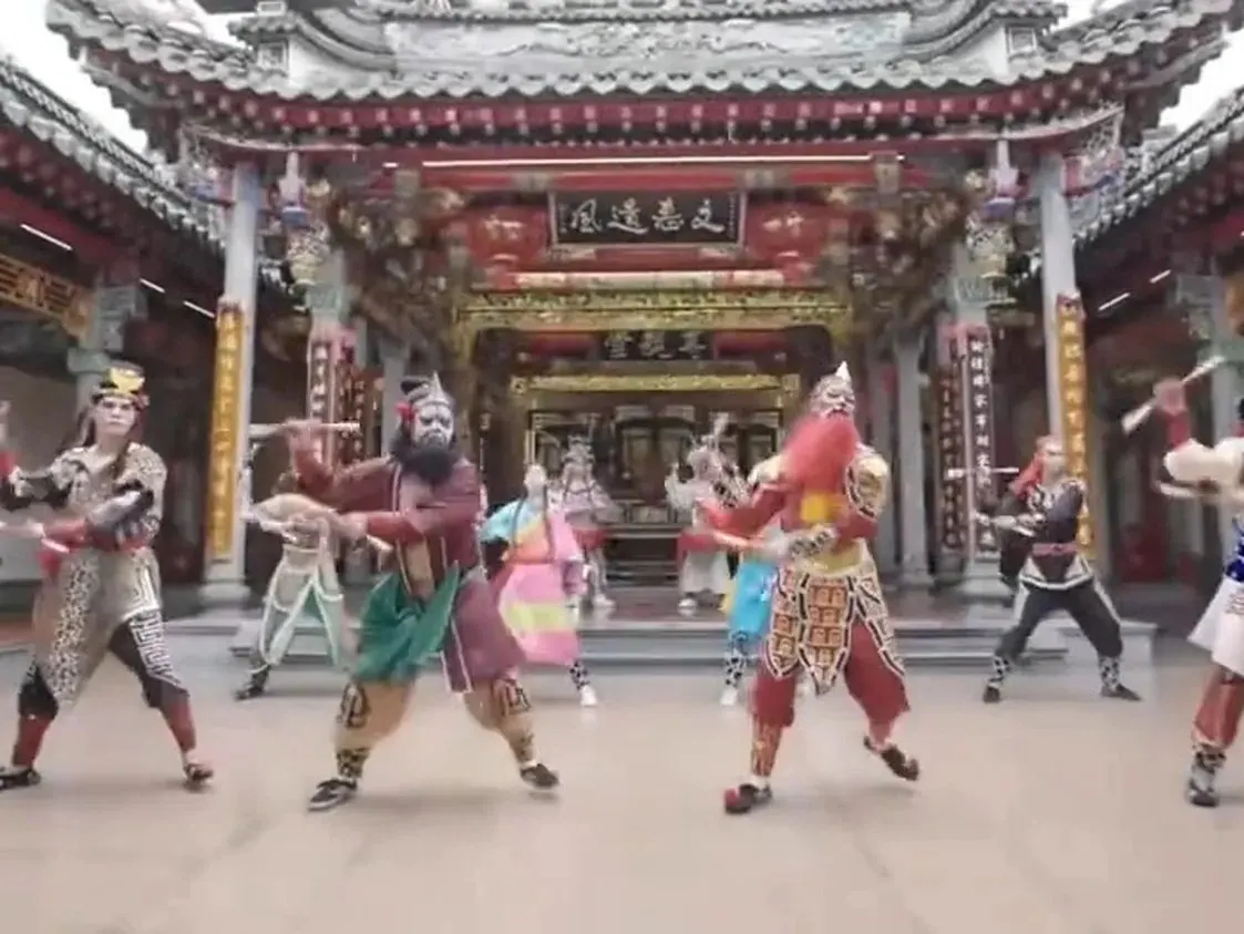 廟前天井，一隊人在演，門楣匾額橫在樑上