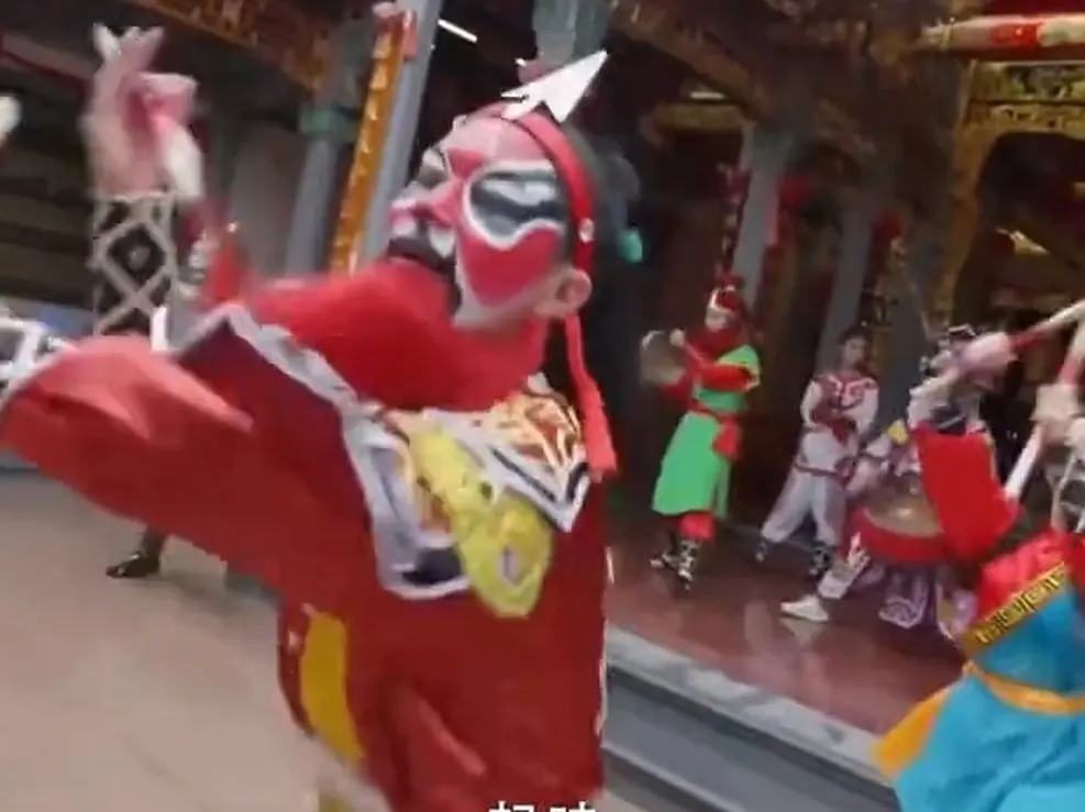 廟前一名紅臉隊員仰頭舉槌，旁邊有人打鈸