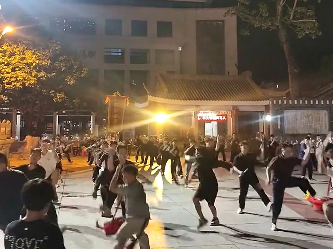 夜裡廣場，幾十名未換戲服的隊員在練槌，路燈拉出長影
