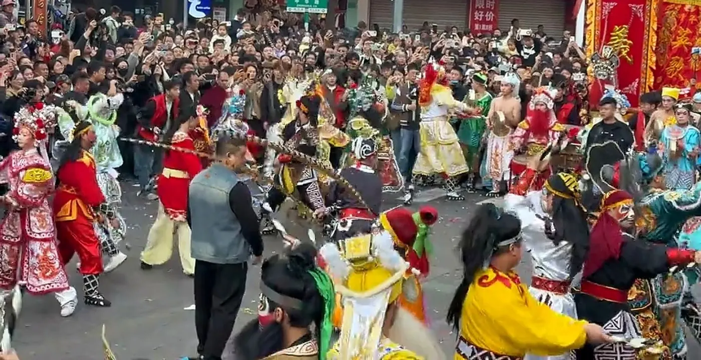 潮阳英歌，队员勾脸持槌在街心推进，身后是围观的街坊