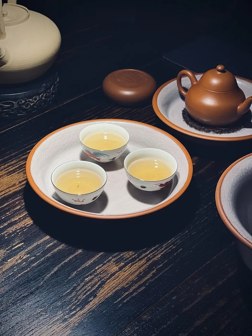 白色茶盘上三只小杯盛着茶汤,旁有紫砂壶与茶罐