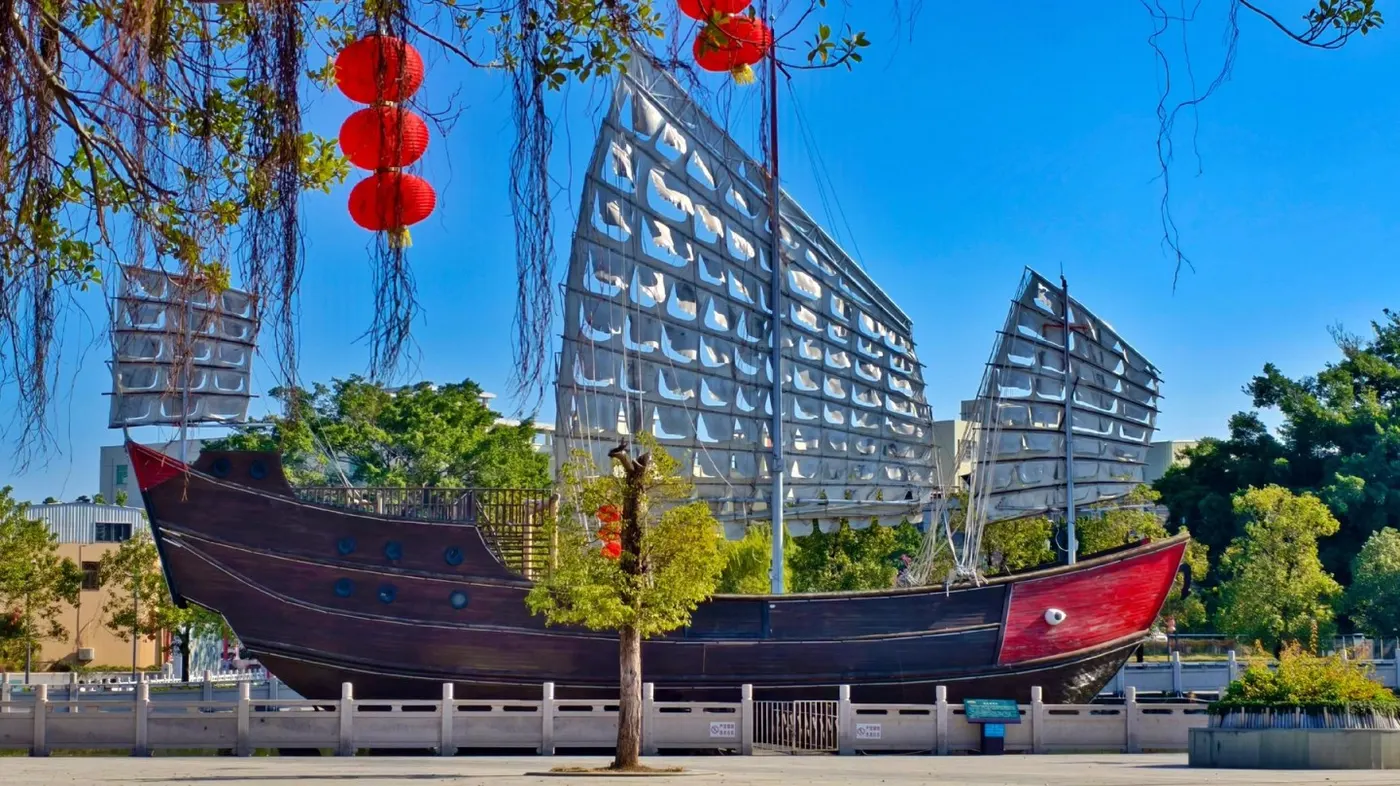 红头船立在广场上,背后是现代住宅楼与红灯笼